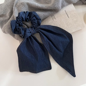 Large dark blue denim bow scrunchie with brown stitching on minimalist grey background