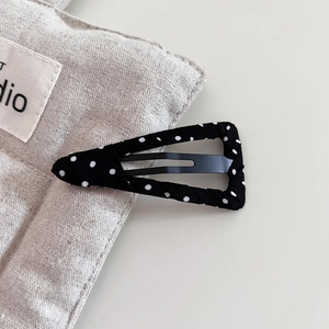 Detailed view of black polka dot fabric covered cloud hair clip on a linen bag