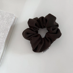 Detail of dark brown ribbed corduroy scrunchie texture with a small white brand tag