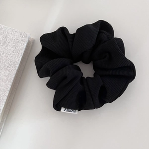 Detailed close-up of a black corduroy scrunchie with a small white woven brand tag on it