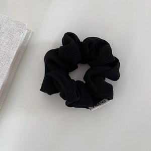 Detailed view of black corduroy scrunchie fabric texture with minimalist woven brand label