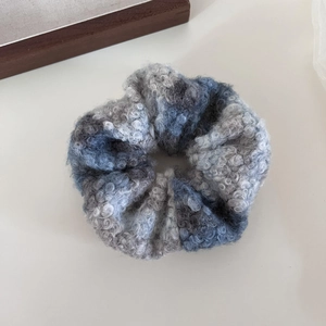 Détail du chouchou en laine douce à carreaux montrant la texture tricotée bleue et grise