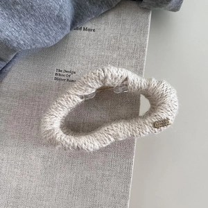 Detailaufnahme der Strick-Haarklammer mit beigefarbener Wolle und LOVEDAYS-Metallemblem