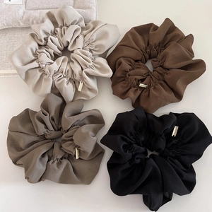 Close-up of four large earth-tone scrunchies in beige and brown with gold metal tags