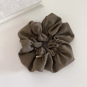 Macro detail of brown oversized scrunchie with a gold metal handmade tag and soft fabric folds