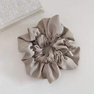 Detail of greige satin scrunchie featuring a premium rectangular silver metal tag