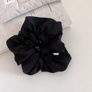 Detail of a black silk scrunchie with a silver handmade metal plate on a book background