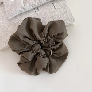 Elegant large brown fabric hair scrunchie with a gold metal tag on a textured background