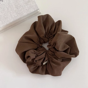Detailed macro view of the premium brown satin scrunchie with a golden logo tag