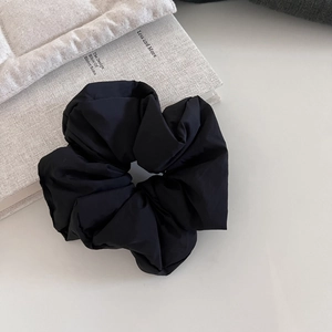 Close-up of a black oversized puffy scrunchie on a gray book with textured fabric