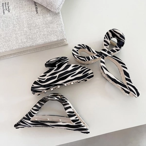 Three zebra print hair claws in bow, crescent, and triangle shapes on a minimal background