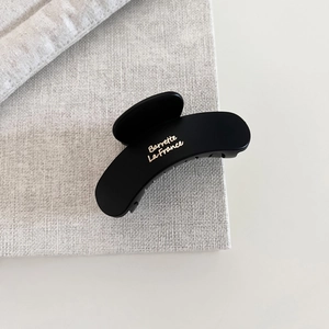 Detail of matte black French hair claw with gold lettering on a linen texture
