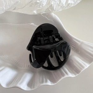 Minimalist black triangular hair claw clip on a white shell plate for elegant hairstyling
