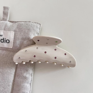 Detailed view of beige acetate hair claw clip with colorful rhinestones on canvas