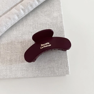 Matte burgundy hair claw clip with golden French lettering on grey textured fabric