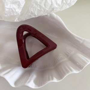 Macro shot of a dark red triangular hair claw clip placed on a white shell porcelain plate