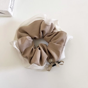 Dettaglio di scrunchie a strati in tessuto kaki e organza bianca con fiocco e ciondolo in metallo