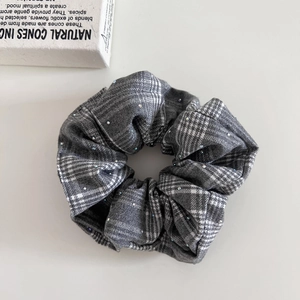 Détail d'un chouchou à carreaux gris avec des strass étincelants sur fond blanc