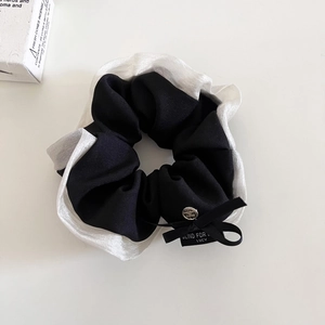Dettaglio dello scrunchie con fiocco, testo Blind For Love e pendente in argento