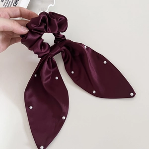 Detailed close-up of wine red satin scrunchie with white pearls and long ribbon tails