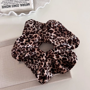 Chouchou en velours à motif léopard avec plis élastiques sur un plateau en tissu gris