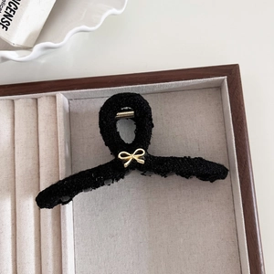 Dettaglio della pinza per capelli in tweed nero con fiocco dorato su vassoio di velluto