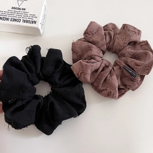 Detail of distressed fabric hair scrunchies in black and grey-purple with slogan label