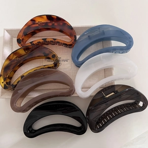 Close-up of seven assorted tortoiseshell and acetate crescent hair claw clips on a beige tray