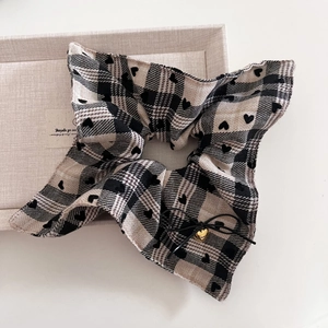 Close-up of black and white plaid scrunchie with heart pattern and gold heart charm
