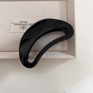 Detail view of a black hollowed-out crescent hair claw clip on a beige textured fabric tray