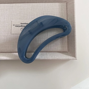 Close-up of deep blue tortoiseshell claw clip in crescent hollow design on beige fabric
