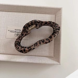 Detail view of large leopard print hair claw clip with golden spring on linen tray