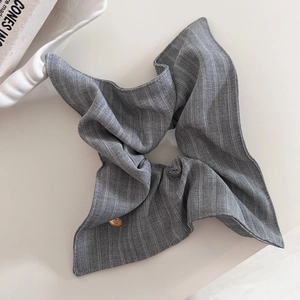 Détail d'un chouchou en tissu gris rayé avec une plaque logo ronde en métal doré