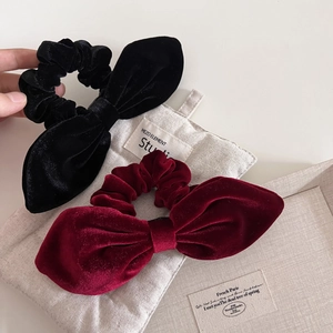 Detail view of black and wine red velvet bunny ear scrunchies on a soft linen background
