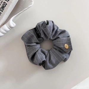 Détail d'un chouchou à carreaux gris avec étiquette tissée et breloque dorée chic