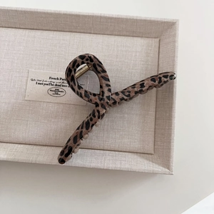 Close-up of vintage leopard print hair claw clip with golden metal spring on beige tray