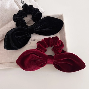 Close-up of velvet bow scrunchies in black and burgundy on a beige linen tray