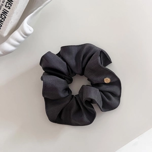 Détail d'un chouchou en tissu rayé gris foncé avec un petit charme en métal doré