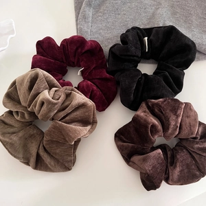 Close-up of four velvet corduroy scrunchies in deep red, black, coffee and tan colors