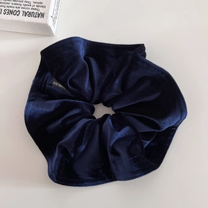Detail of navy blue velvet scrunchie showing premium texture and branded label