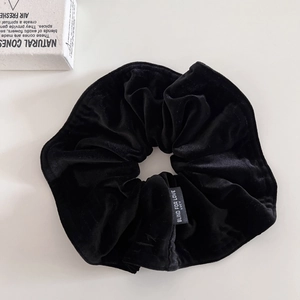 Detailed view of black velvet scrunchie texture with white printed brand label