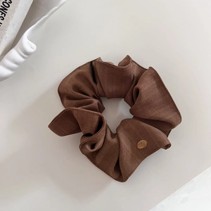 Vue détaillée du chouchou rayé marron avec une étiquette en métal doré sur fond beige