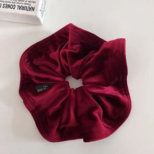 Detailed close-up of premium red velvet hair scrunchie with fine stitching and label