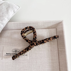 Detail of elegant large leopard print hair claw clip in beige textured display tray
