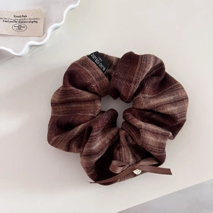 Plaid scrunchie with brown ribbon bow and silver heart pendant on textured fabric