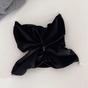 Elegant black velvet hair scrunchie with pearl accents and bow-style design on beige background