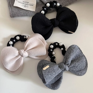 Detailed view of three pearl-decorated wool bow hair ties in black, beige and grey tones