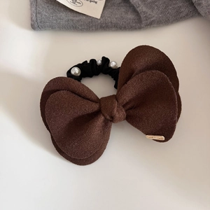 Close-up of brown velvet bow hair tie featuring white pearls and a gold handmade tag