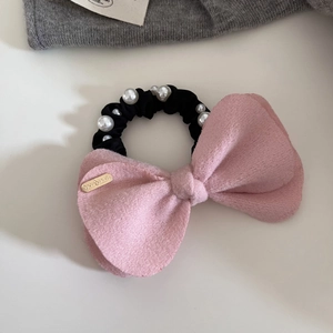 Detail of a pink fuzzy bow hair tie with handmade metal tag and white pearl accents