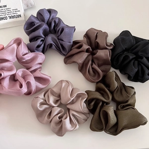 Detail of six satin scrunchies in purple, brown, pink, and olive green with shiny textures
